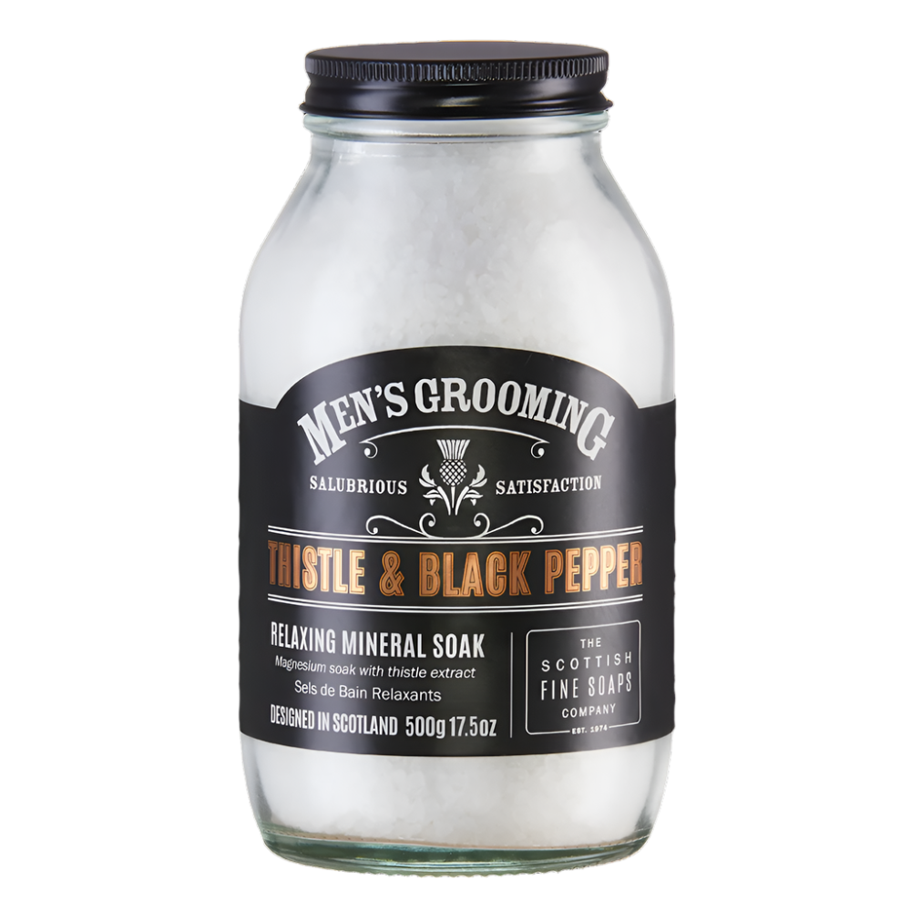 The Scottish Fine Soaps Company Men’s Grooming Bath & Muscle Soak Jar, 500g. A transparent glass jar with a stylish black label featuring the Thistle & Black Pepper design. Contains mineral bath soak.